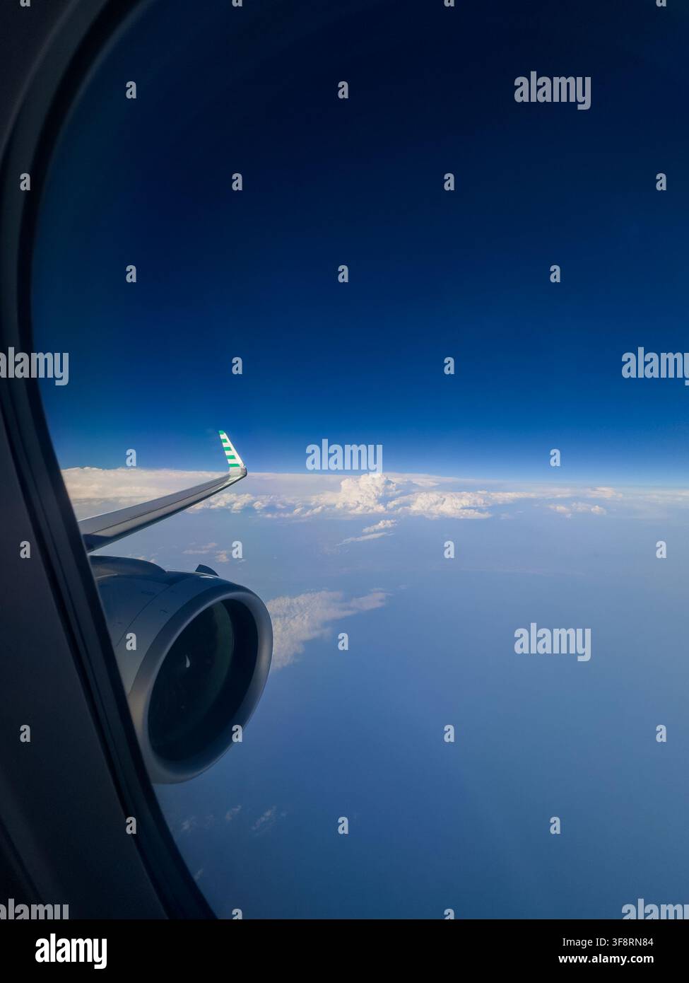 Vue depuis une fenêtre d'avion montrant un moteur à réaction et un aile au-dessus d'un vaste océan bleu et d'une couche de nuages Banque D'Images