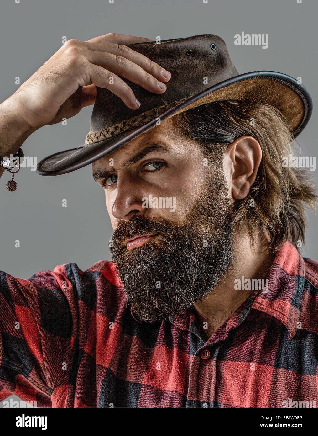 Homme ajustant son chapeau de cowboy. Cowboy mal rasé. Cowboy américain. Style cowboy en chemise à carreaux Banque D'Images