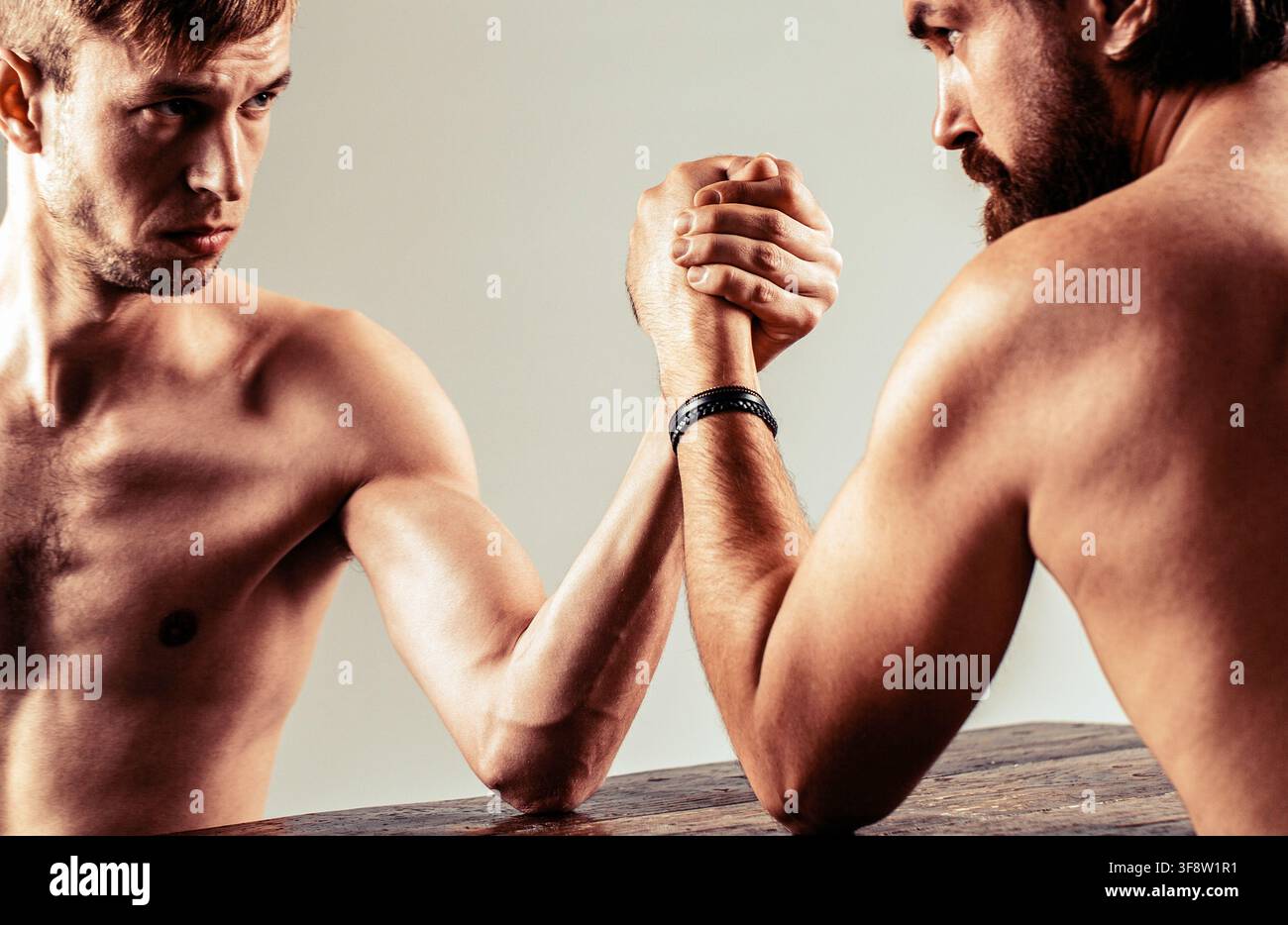 Poignée de main mince, bras grand et fort. Fort et faible, match inégal. Homme barbu fortement musclé faisant un bras de fer avec un homme chétif et faible Banque D'Images