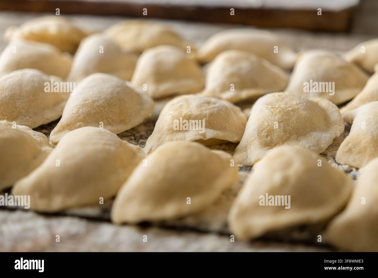 Des pâtes de pâte non cuites sont disposées sur une légère couche de farine sur une planche sombre, mettant en valeur l'artisanat de la préparation alimentaire faite à la main pour Banque D'Images