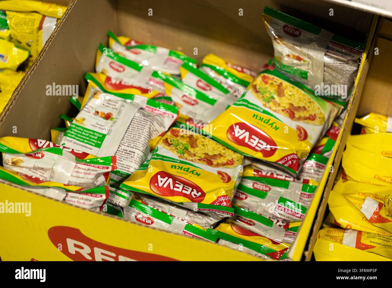 Horodok, Ukraine – 23 mars 2026 : Nouilles emballées Reeva organisées dans une caisse en carton dans une boutique de détail, mettant en valeur les aliments de convenience produits en masse Banque D'Images