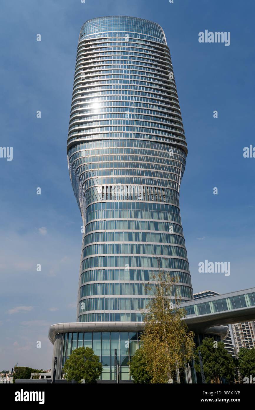 Une vue en contre-plongée d'un gratte-ciel moderne en verre torsadé s'élevant dans un ciel bleu clair à Belgrade, en Serbie. Le soleil se reflète brillamment sur la façade incurvée Banque D'Images