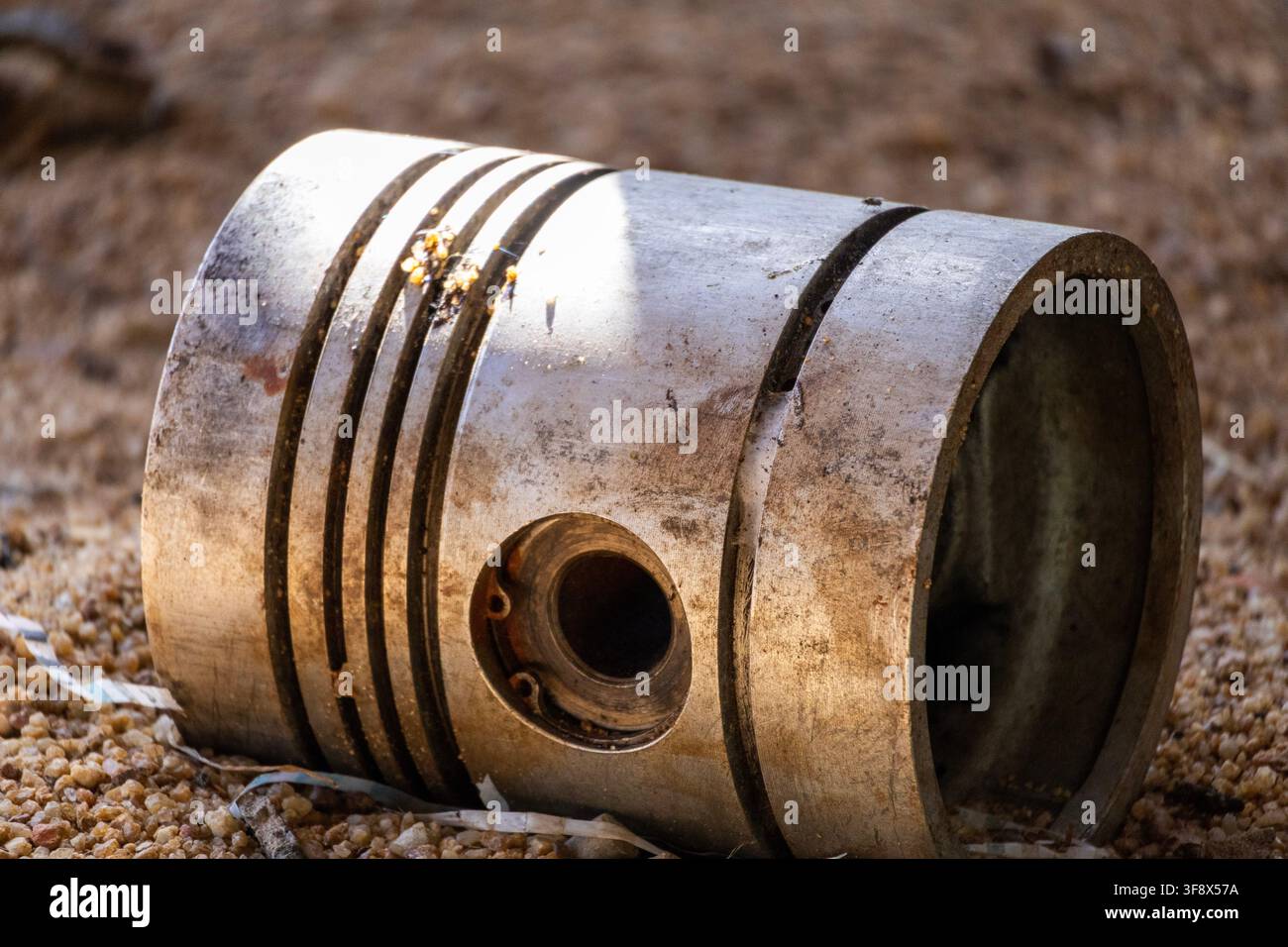 Piston de moteur diesel abandonné reposant au sol avec la lumière du soleil qui l'illumine au coucher du soleil Banque D'Images