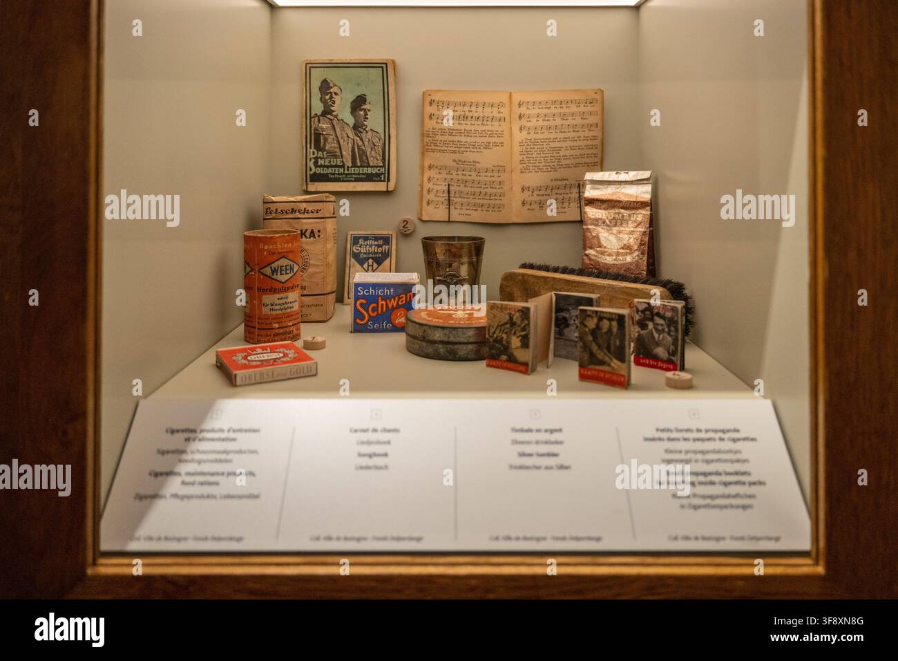 Bastogne, Belgique - 21 juil. 25 : Vitrine contenant des livres allemands de l'époque de guerre, des produits ménagers et des objets de propagande dans les salles de guerre de Bastogne. Banque D'Images