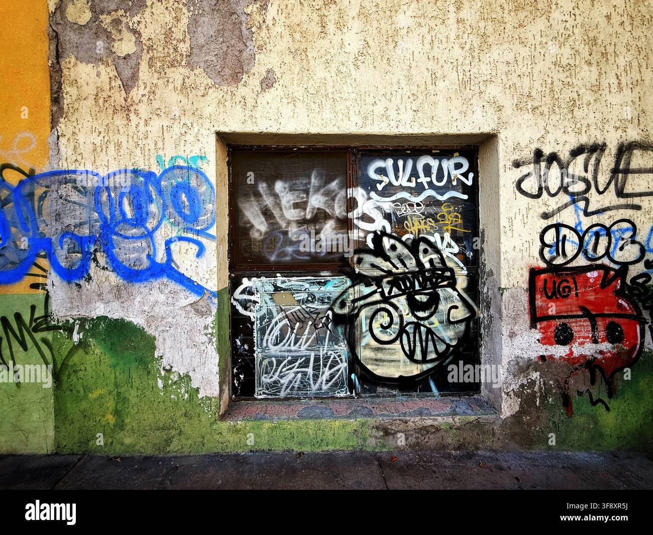 Fenêtre couverte de graffitis dans un mur urbain érodé Banque D'Images