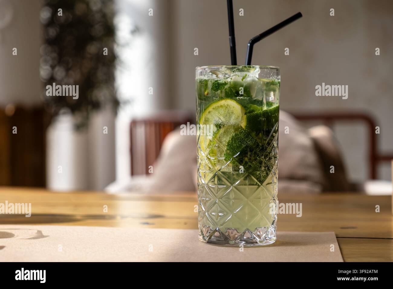 Un mojito glacé servi dans un verre highball texturé avec des pailles noires sur une table, capturant l'essence fraîche et savoureuse d'un classique vacat Banque D'Images