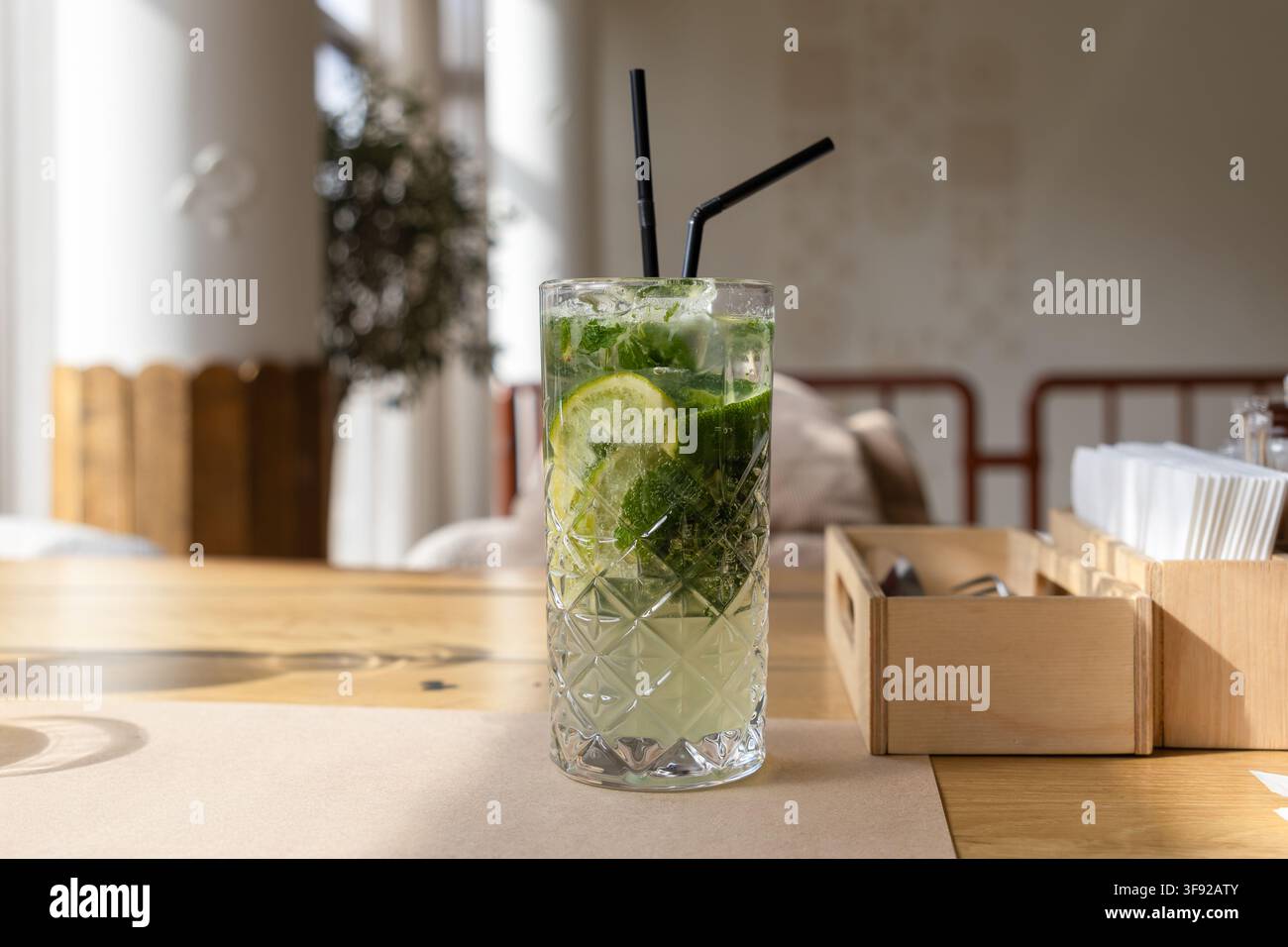 Boisson mojito rafraîchissante remplie de glace, de menthe et de citron vert reposant sur une table en bois chaud dans un café ensoleillé, évoquant une atmosphère estivale fraîche pour l'hospitalité Banque D'Images