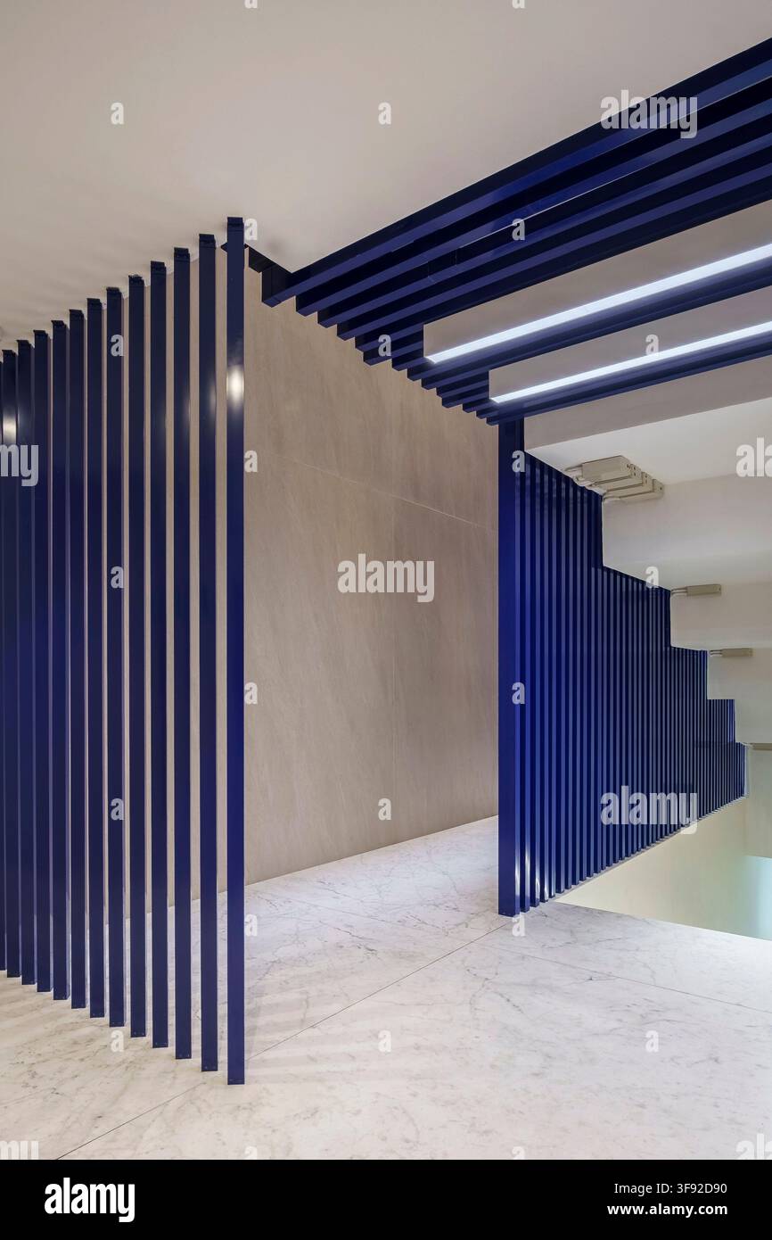 Perspective intérieure architecturale montrant un design de couloir contemporain avec des cloisons verticales à lamelles bleu foncé audacieuses s'étendant jusqu'au plafond. Banque D'Images