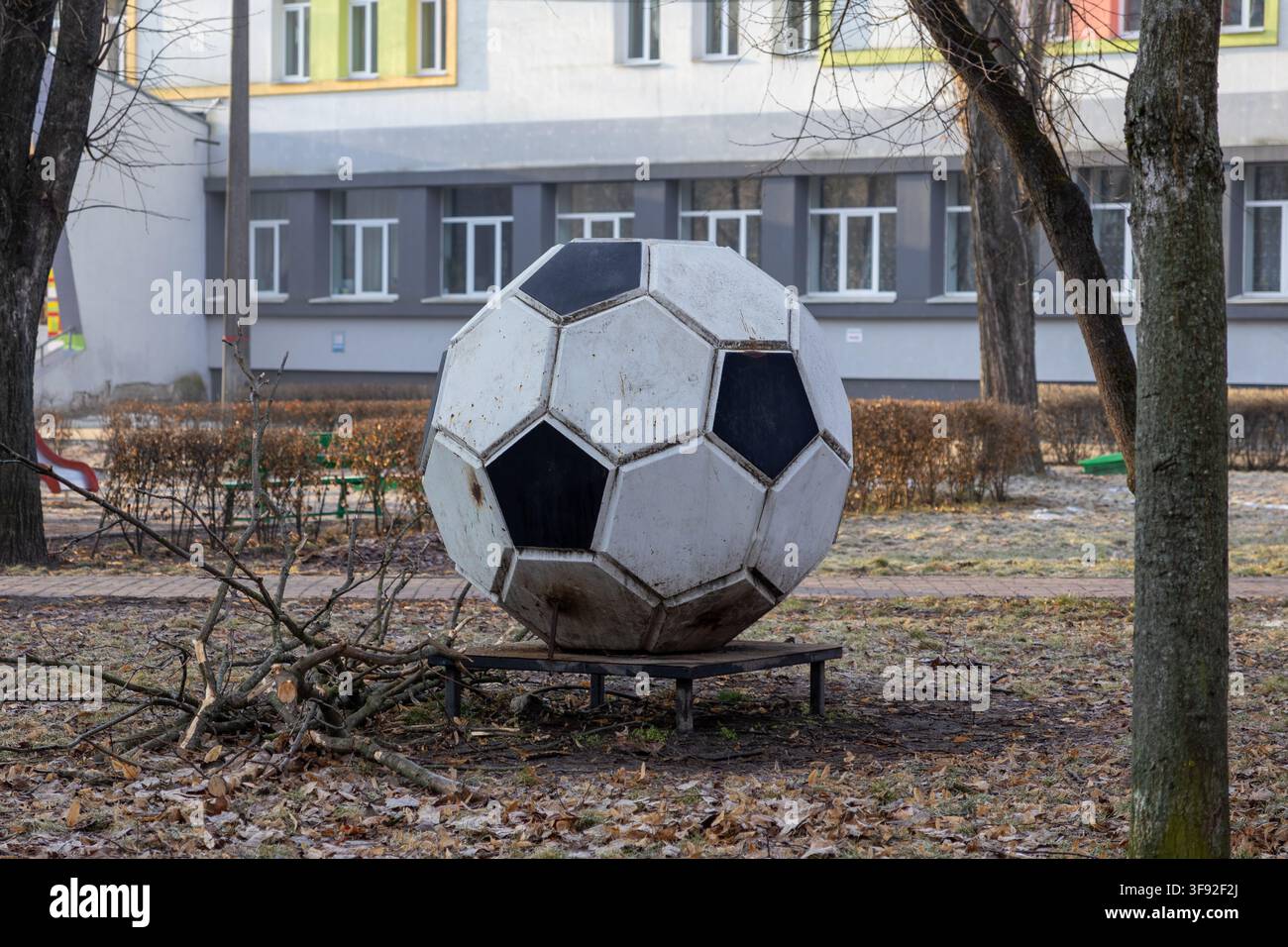 Décoration en acier patiné en forme de ballon de football placée dans une cour d'école entourée d'arbres et de feuilles mortes tombées, évoquant des thèmes d'énergie juvénile et d'éducation physique Banque D'Images