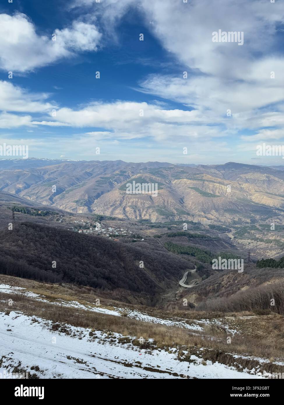 Paysage montagneux avec route sinueuse et plaques de neige sous un ciel bleu éclatant. Banque D'Images
