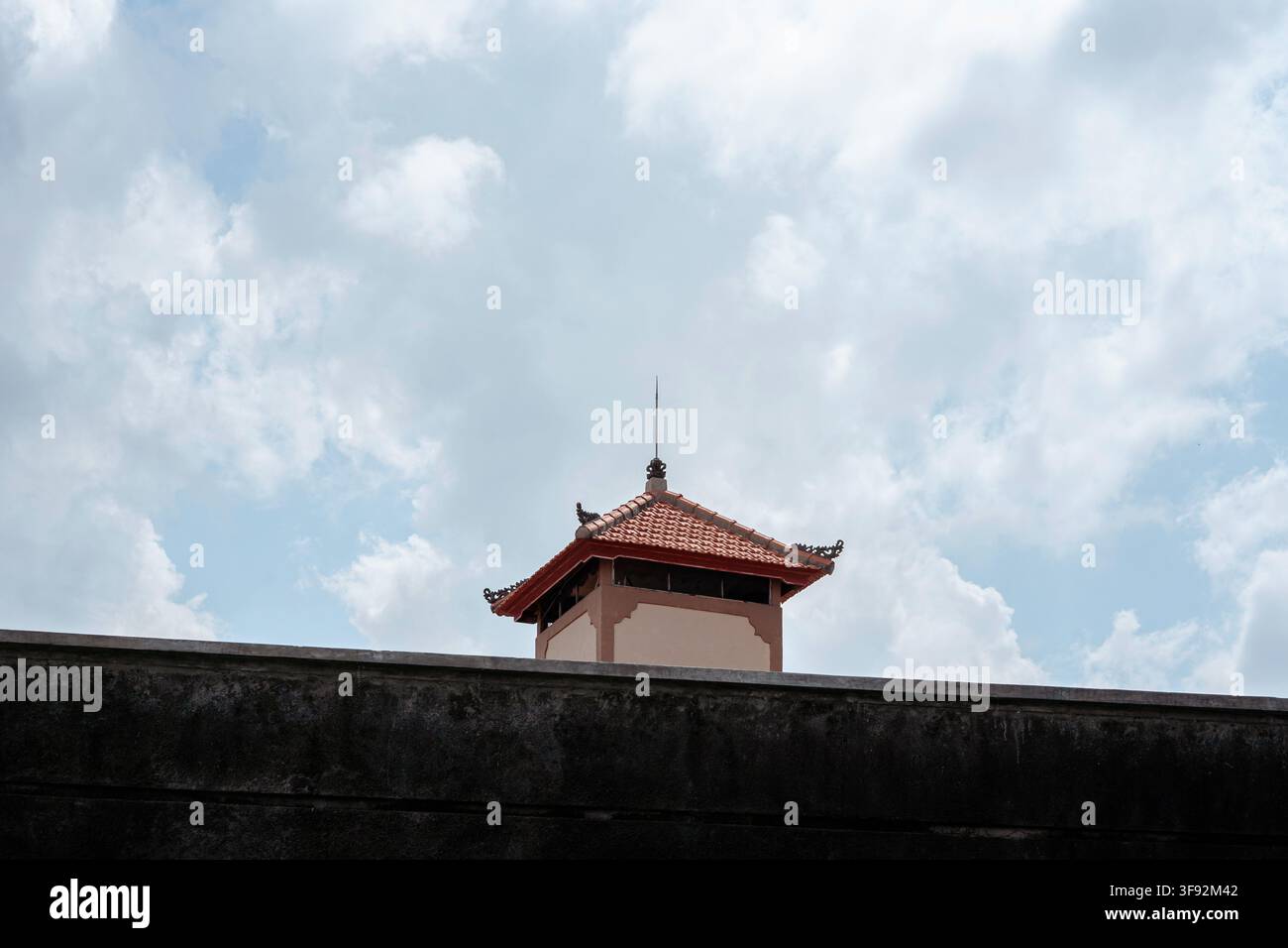 Prise de vue en contre-plongée d'un toit de tour décoratif avec un clocheton au sommet d'un mur érodé, sur fond de ciel nuageux. Banque D'Images