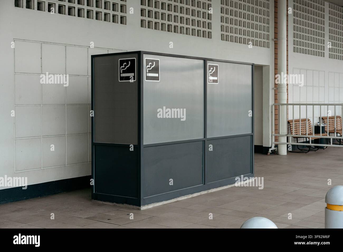 Abri moderne désigné pour fumer en extérieur avec cadre en métal sombre, panneaux translucides et panneaux de symboles de fumeur à l'extérieur d'un bâtiment. Banque D'Images