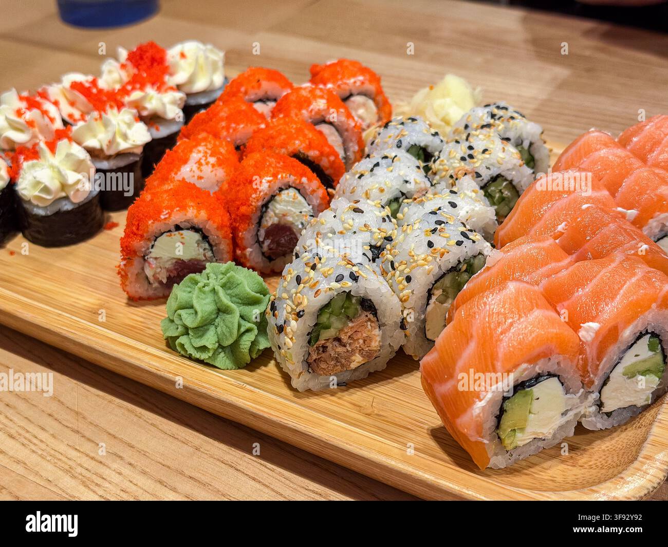 Assiette appétissante de diverses roulades de sushi comprenant du saumon, du fromage à la crème et de la roe de poisson épicée sur une planche de service en bois pour mettre en valeur un gourmet sain Banque D'Images