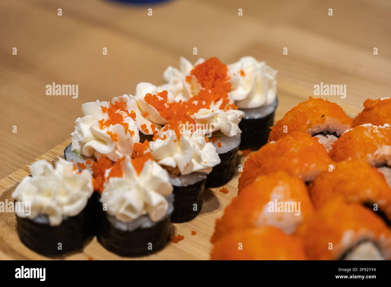 Variété de sushi appétissante garnie de délicates spirales de crème et d'œufs de poisson vibrants, présentée sur un plateau en bois naturel, mettant en valeur un art culinaire authentique Banque D'Images