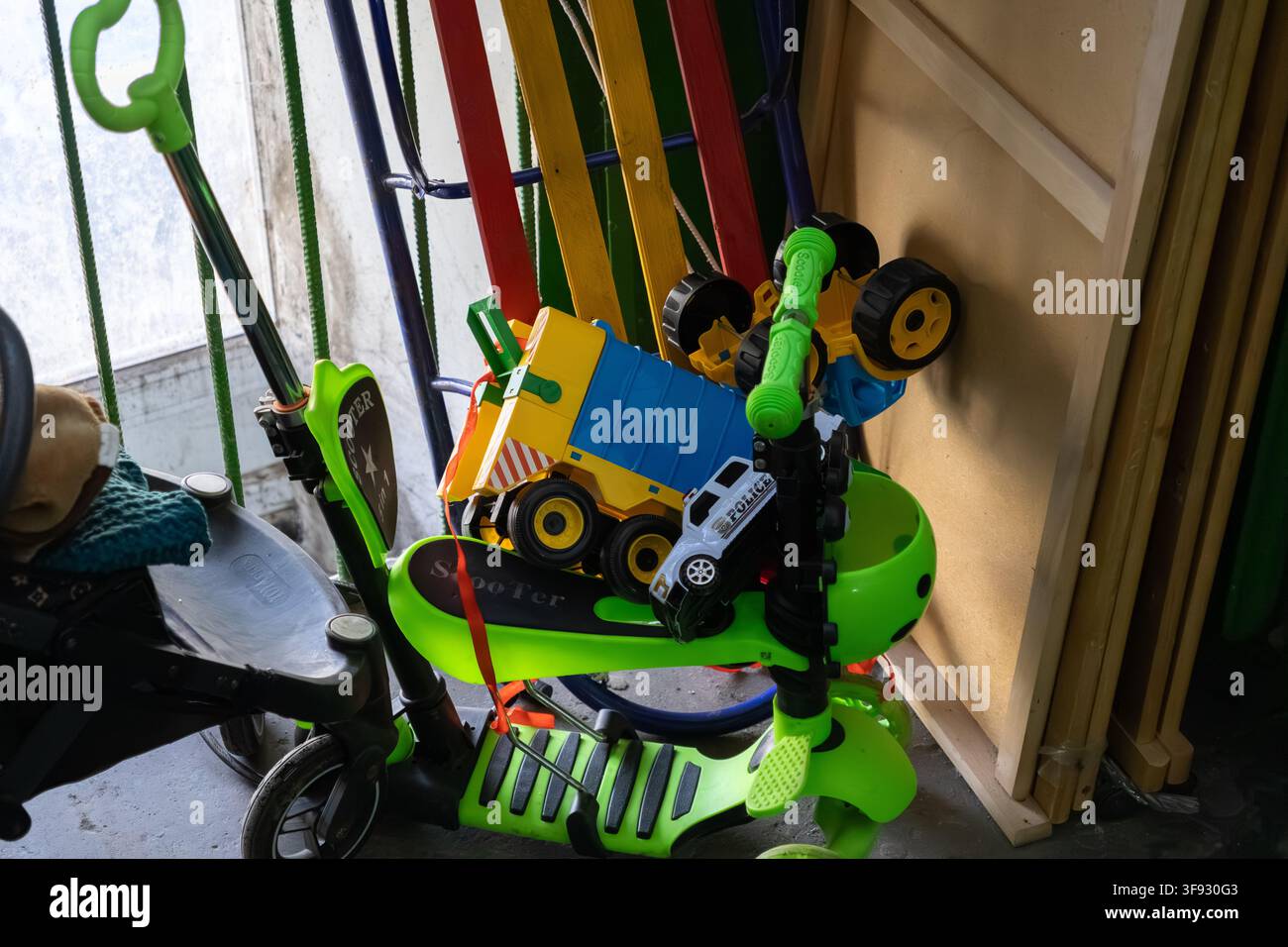 Des véhicules-jouets aux couleurs vives et une trottinette verte empilés dans un débarras désordonné, représentant les souvenirs d'enfance et la nature chaotique d'une organisation Banque D'Images