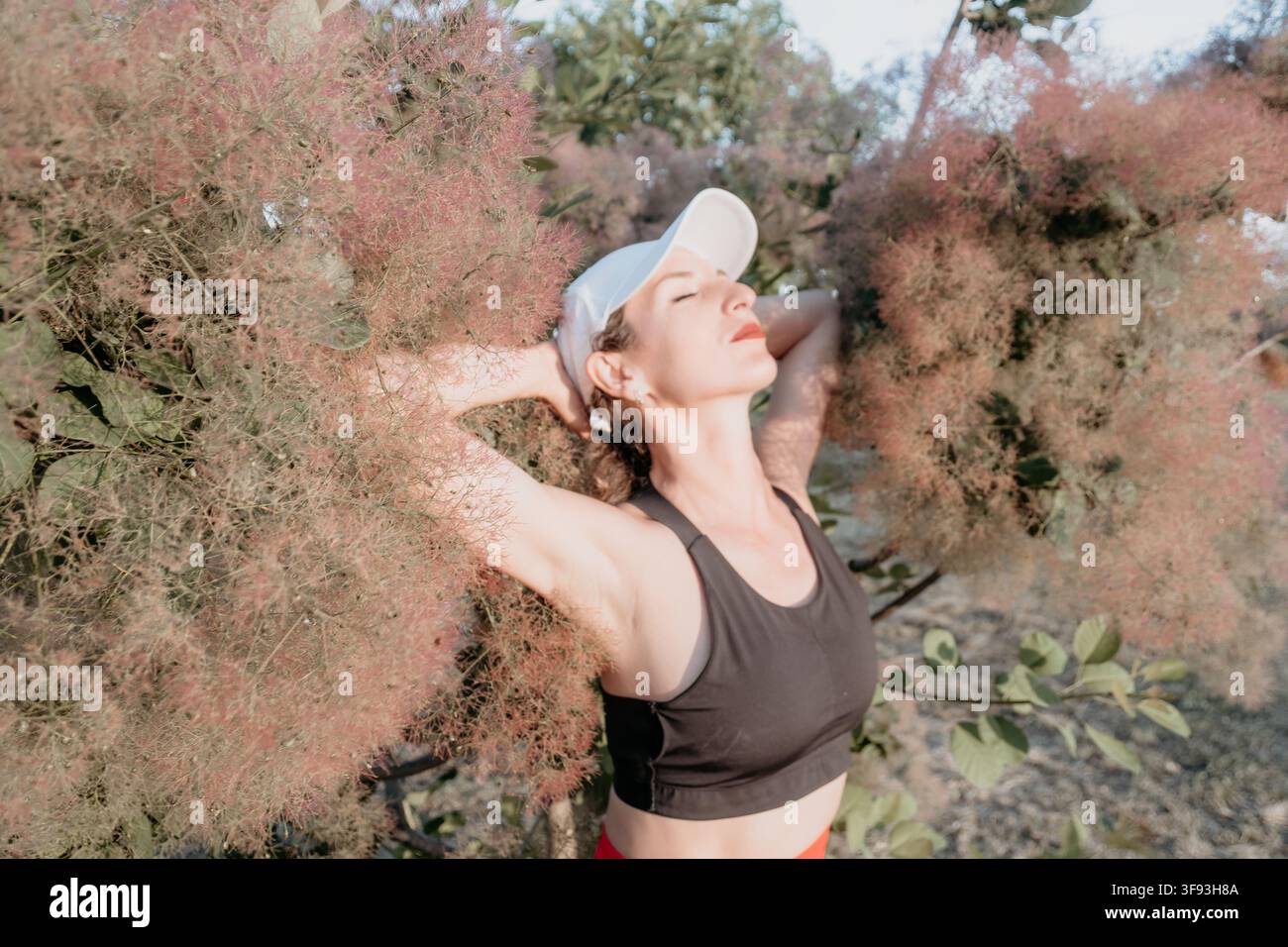 Style de vie fitness, femme athlétique en vêtements de sport se détendant près d'un buisson en fleurs en plein air par une journée ensoleillée Banque D'Images