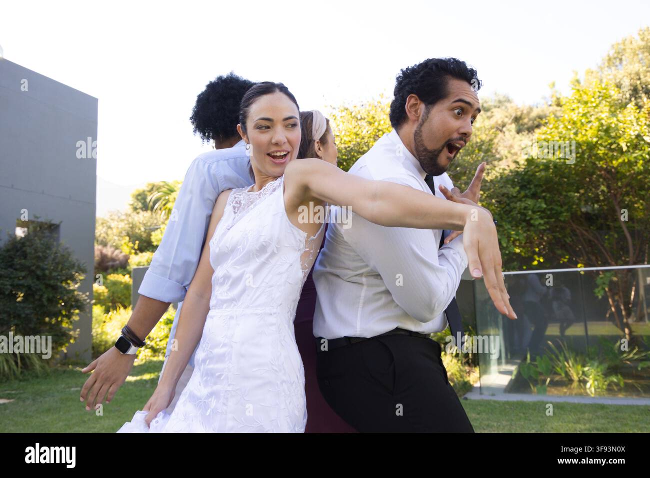 Groupe de mariage divers posant dos à dos, la mariée en robe de dentelle blanche souriant sur une pelouse bien entretenue Banque D'Images
