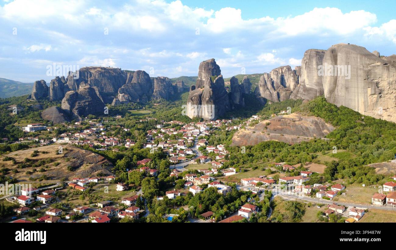 Vue aérienne des impressionnants piliers rocheux des Météores dominant un village grec pittoresque niché parmi des collines verdoyantes. Banque D'Images