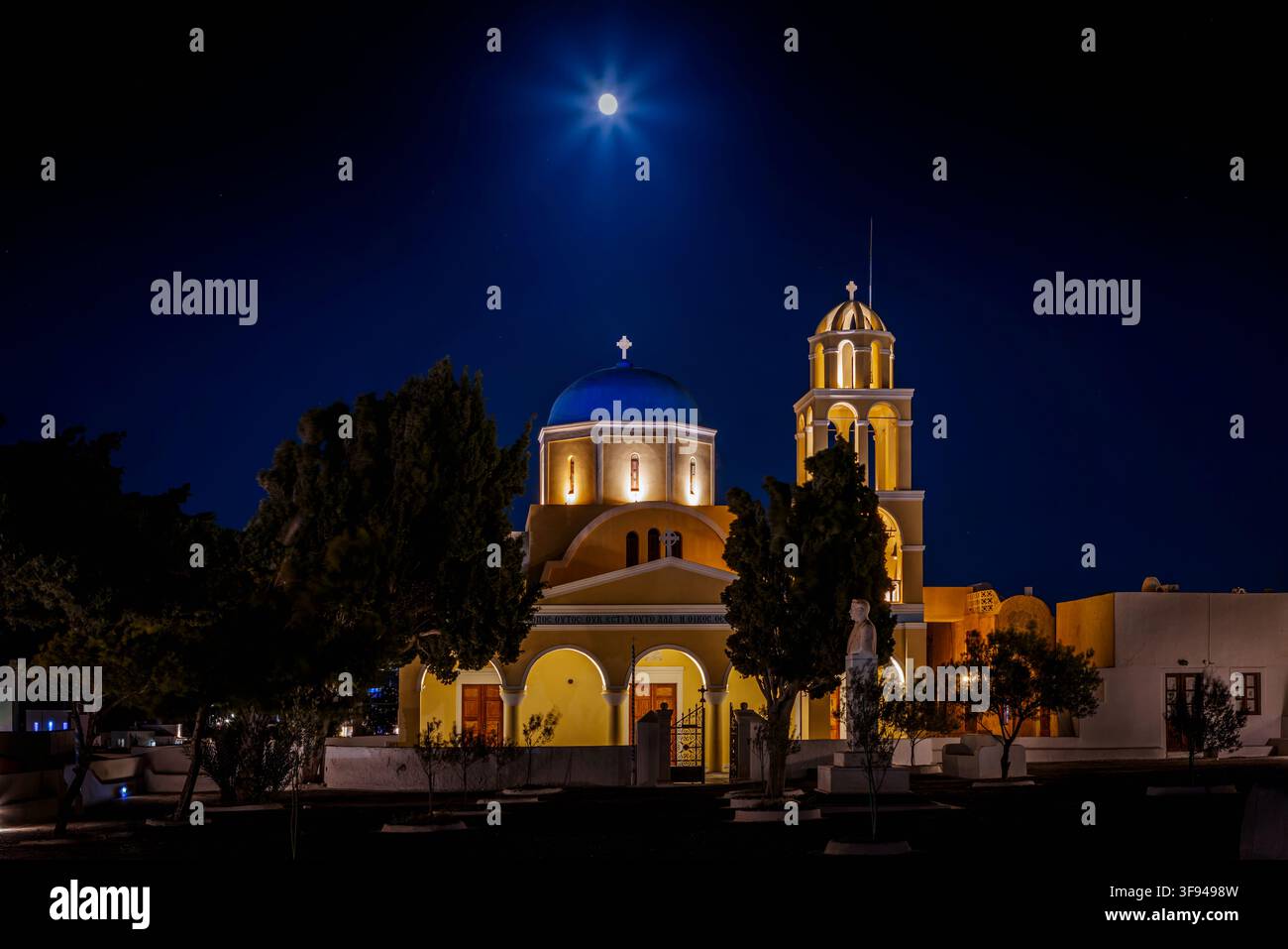 Lune brillant au-dessus de l'église Agios Georgios illuminée la nuit dans le village d'Oia sur l'île grecque de Santorin. Banque D'Images