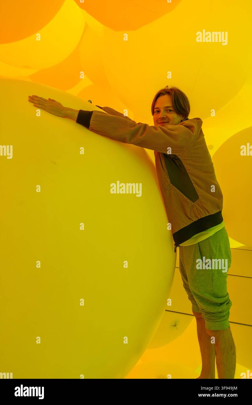 Un touriste souriant pose avec de grandes sphères jaunes lumineuses à l'intérieur d'une installation interactive à teamLab Planets à Tokyo, au Japon. Banque D'Images