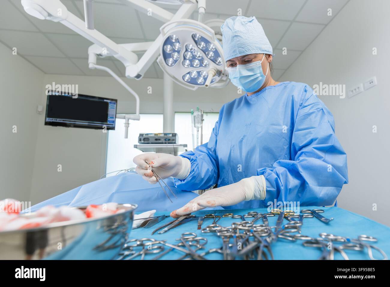 Une chirurgienne organise des instruments chirurgicaux sur une table dans une salle d'opération. L'atmosphère suggère une préparation pour une opération. Banque D'Images