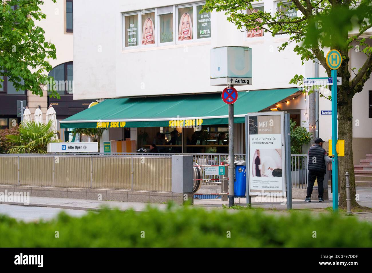 Une vue au niveau de la rue de l'entrée de la station de métro Alte Oper à Berlin, avec un auvent vert pour un café « Sunny Side Up » et une personne attendant à une Banque D'Images