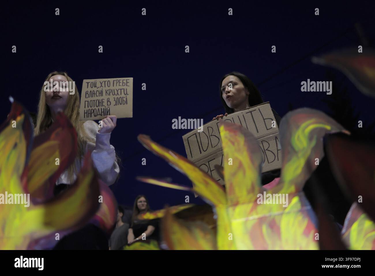 Deux femmes tiennent des panneaux en carton lors d'une manifestation sur la Place de la Liberté (Площа Свободи) à Kharkiv, en Ukraine, le 14 août 2026. Le panneau de gauche porte en ukrainien : "Той, хто гребе власні крихти, потоне в злобі народній" ("Celui qui amasse ses propres miettes se noiera dans la colère du peuple"); le panneau partiellement caché à droite indique "Поверніть [Федо]рова" ("Rendez [Fedo]rov"), alors que les participants appelaient au rétablissement de Mykhailo Fedorov comme ministre de la Défense, le 29e jour des manifestations continues à l'échelle nationale contre son renvoi. Banque D'Images