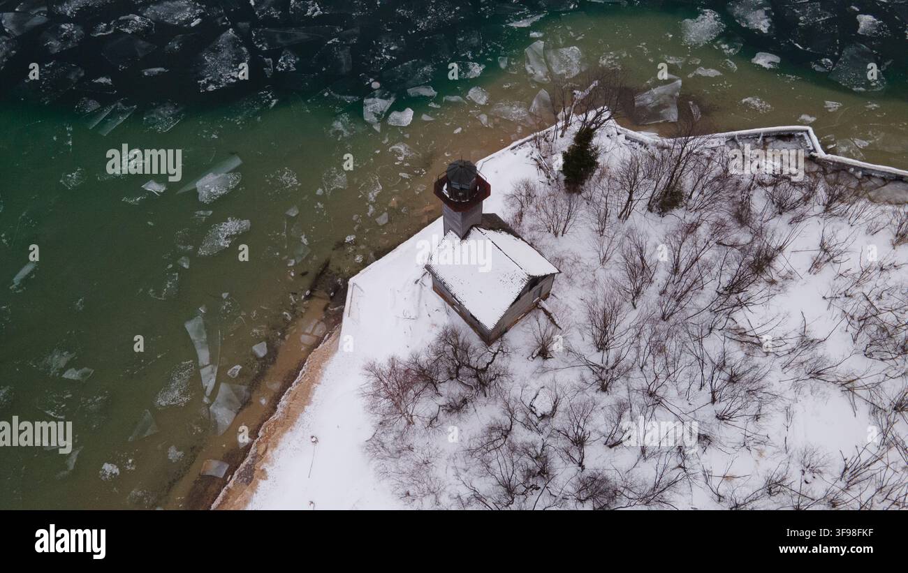 Vue aérienne du phare de Grand Island entouré d'arbres enneigés et des eaux gelées du lac Supérieur à Munising, Michigan, États-Unis. Banque D'Images