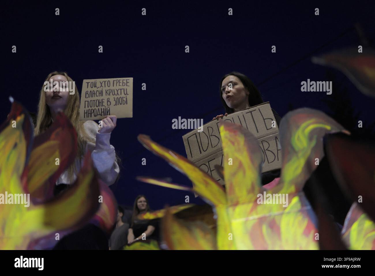 Deux femmes tiennent des panneaux en carton lors d'une manifestation sur la Place de la Liberté (Площа Свободи) à Kharkiv, en Ukraine, le 14 août 2026. Le panneau de gauche porte en ukrainien : "Той, хто гребе власні крихти, потоне в злобі народній" ("Celui qui garde ses propres miettes se noiera dans la colère du peuple"); le panneau partiellement caché à droite dit "Поверніть [Федо]рова" ("Rendez [Fedo]rov"), alors que les participants appelaient au rétablissement de Mykhailo Fedorov en tant que ministre de la Défense, le 29e jour de manifestations continues à l'échelle nationale contre son limogeage. Photo de Yevhen Titov/ABACAPRESS.COM Banque D'Images