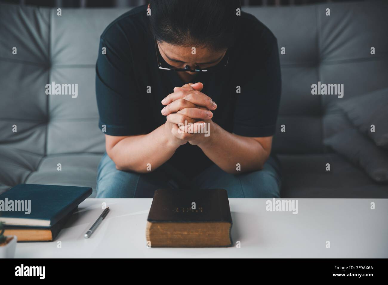 Vue de face en hauteur d'une femme chrétienne d'âge moyen priant les mains jointes au-dessus d'une Bible, représentant la dévotion, la foi, l'espoir, la reddition, un Banque D'Images