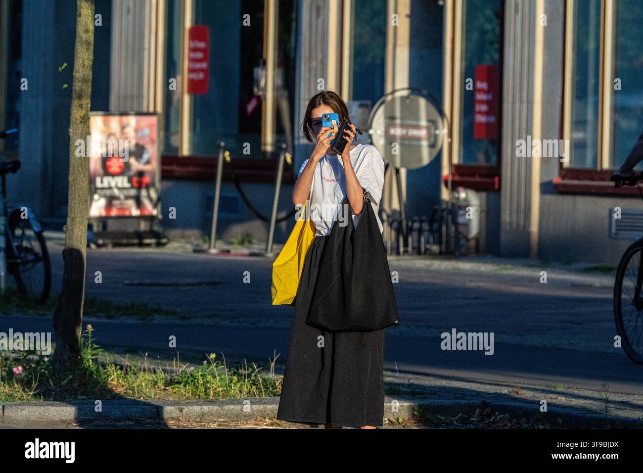 Berlin, Allemagne – 12 août 2026 : Vue d'une femme prenant une photo avec son smartphone sur le trottoir de la Frankfurter Allee à Berlin, en Allemagne. Banque D'Images