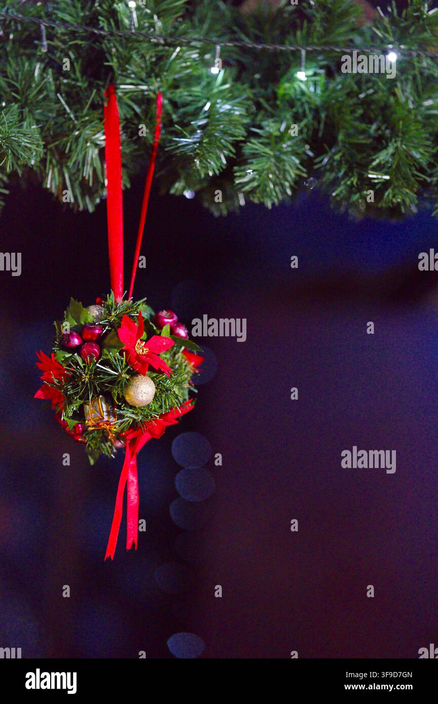 Ornement de Noël suspendu, sur fond sombre intérieur avec effet bokeh, avec sapin de Noël, ornement, vu sous un angle légèrement incliné en gros plan, w Banque D'Images