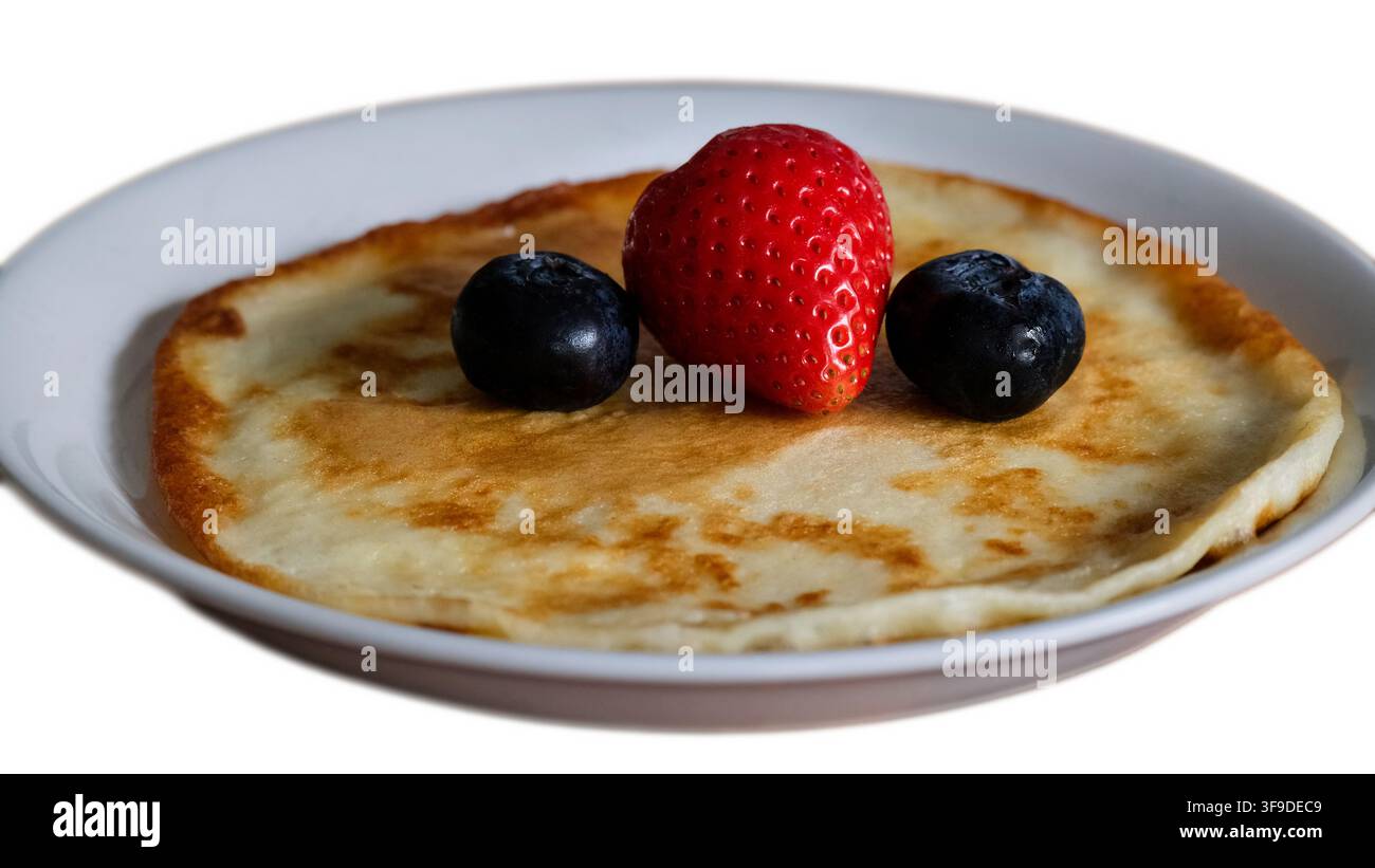 Fine crêpe garnie de fraises rouges fraîches et de myrtilles sur une assiette blanche isolée Banque D'Images