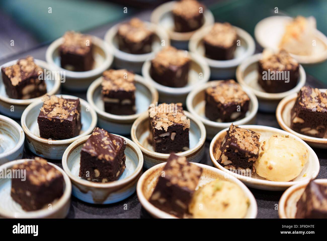 Brownies au chocolat noir riches garnis de noix et de miettes, servis dans de petites coupelles en céramique comme des portions de dessert élégantes lors d'un buffet d'événement de traiteur Banque D'Images