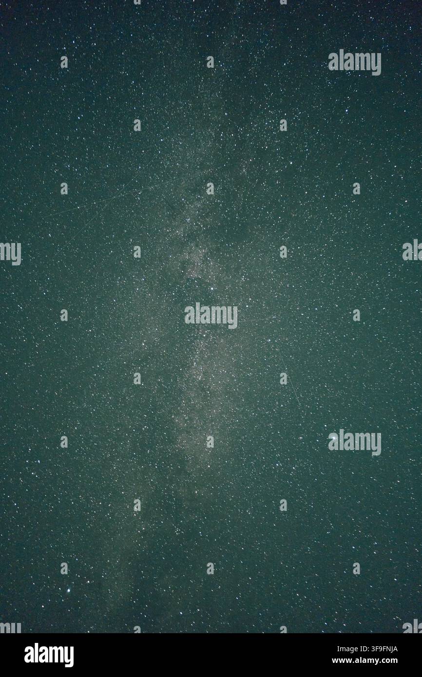Bande verticale de la Voie lactée et champ d'étoiles dense dans un ciel nocturne sombre avec une teinte verte pâle, scène céleste à contraste élevé montrant des points d'étoiles, des lanes de poussière Banque D'Images