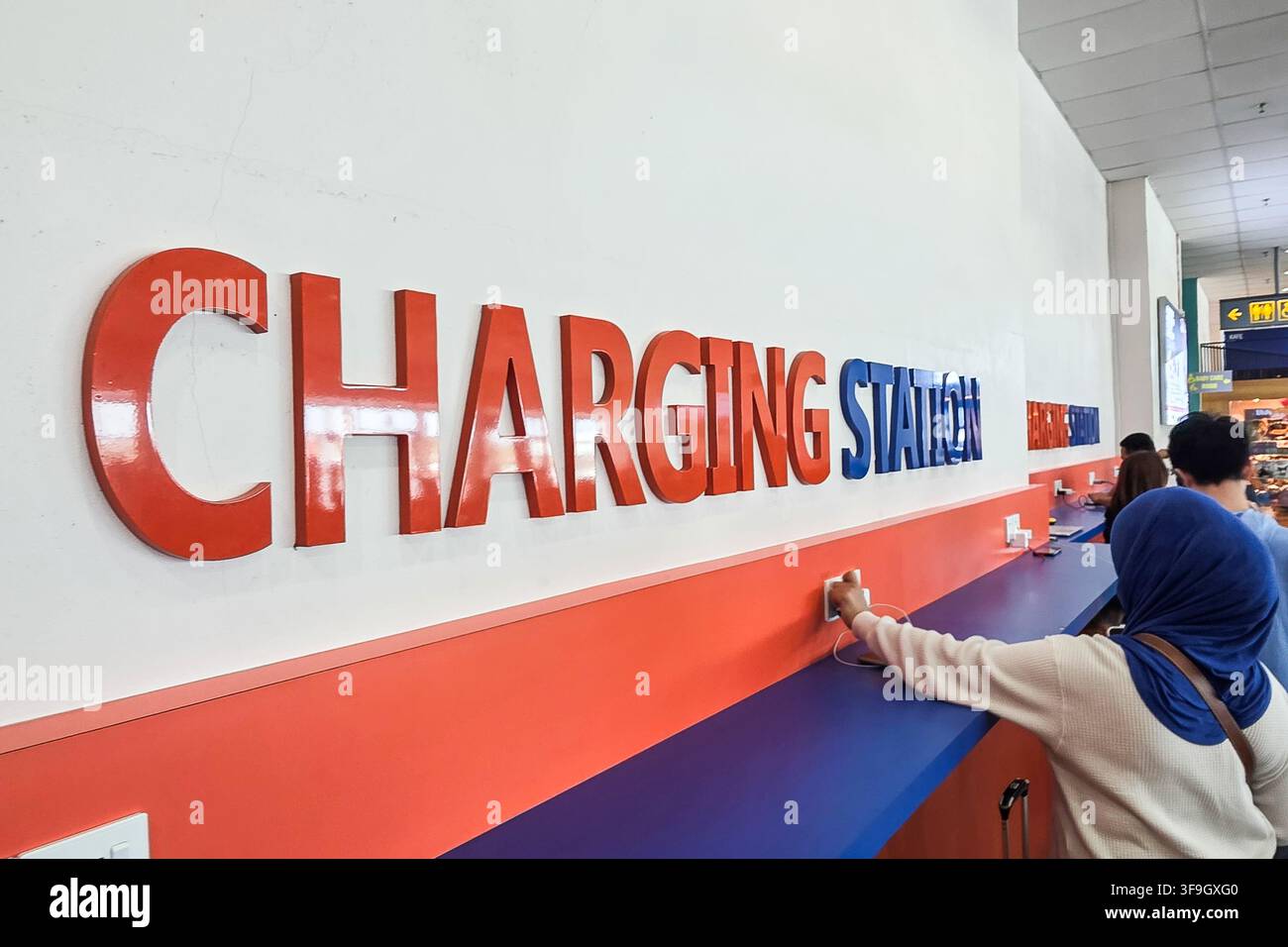 Des voyageurs utilisent une borne de recharge publique gratuite pour leurs téléphones dans le salon d'embarquement de l'aéroport afin de recharger leurs batteries Banque D'Images