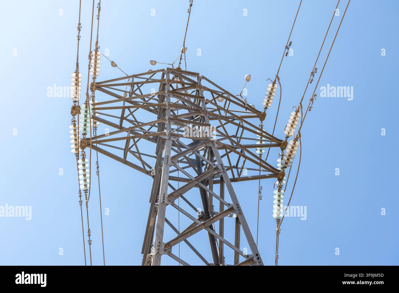 Ce cliché détaillé se concentre sur la structure métallique complexe d'un pylône électrique, mettant en évidence les isolateurs et les câbles devant un ciel clair et sans nuages Banque D'Images