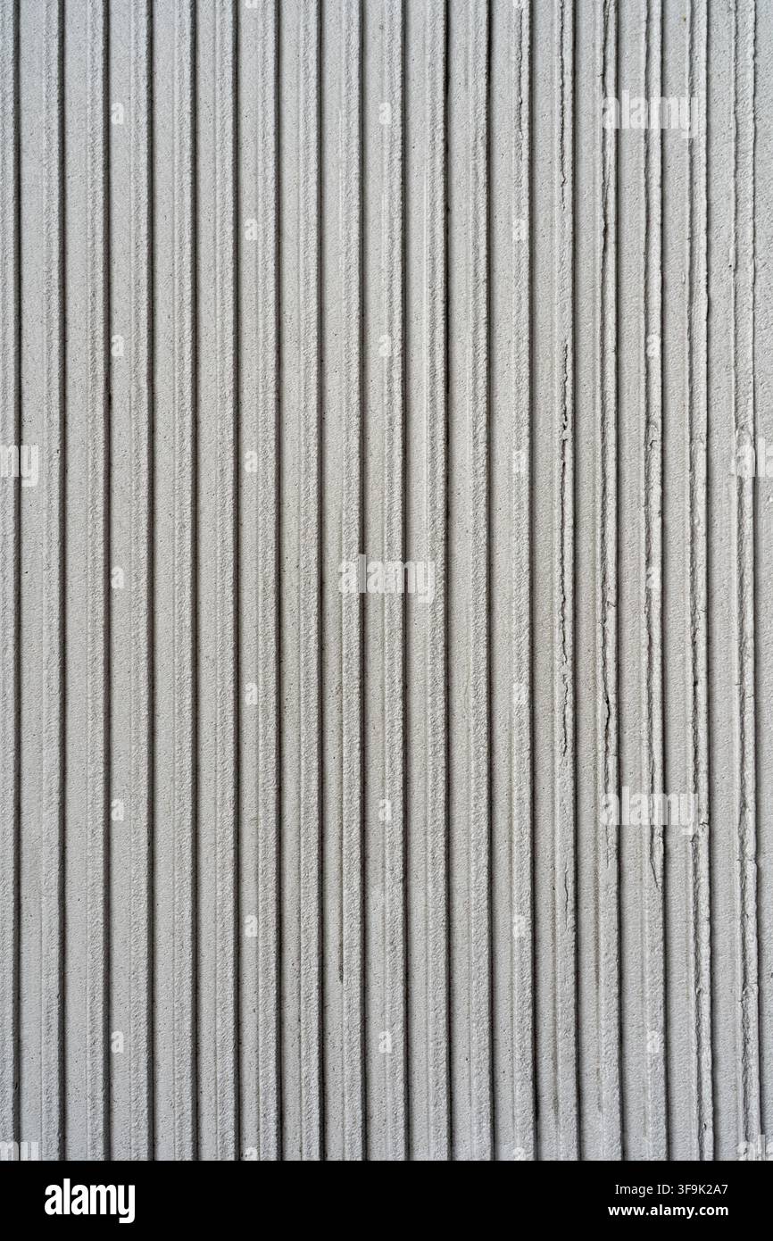 Gros plan d'un mur gris clair texturé avec des rainures verticales étroites, créant un motif de surface architectural minimaliste et un intérieur contemporain Banque D'Images