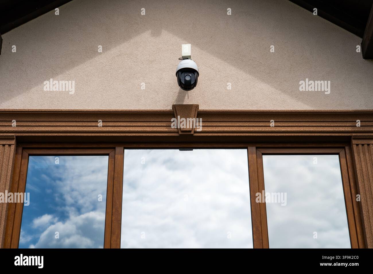 Caméra de sécurité extérieure montée au-dessus des fenêtres de la maison reflétant un ciel nuageux, système de surveillance domestique Banque D'Images