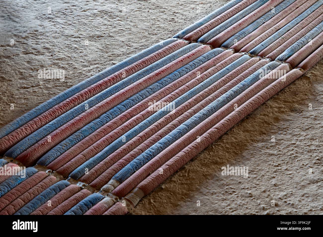 Tubes d'isolation chauffants rouges et bleus disposés en parallèle sur un sol en béton brut d'un chantier de construction Banque D'Images