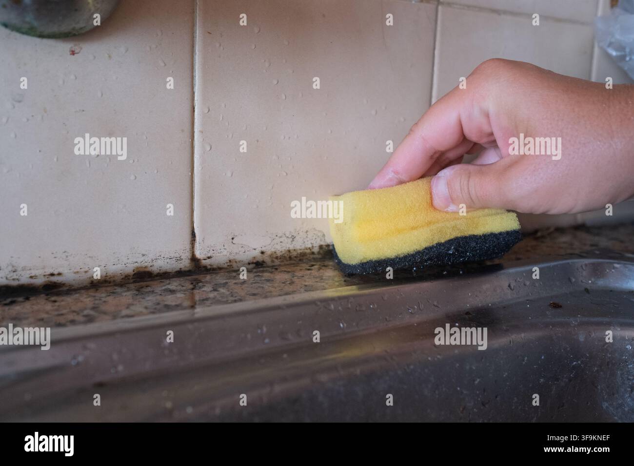 Close-up d'une personne nettoyant les carreaux de l'évier de cuisine avec une éponge Banque D'Images