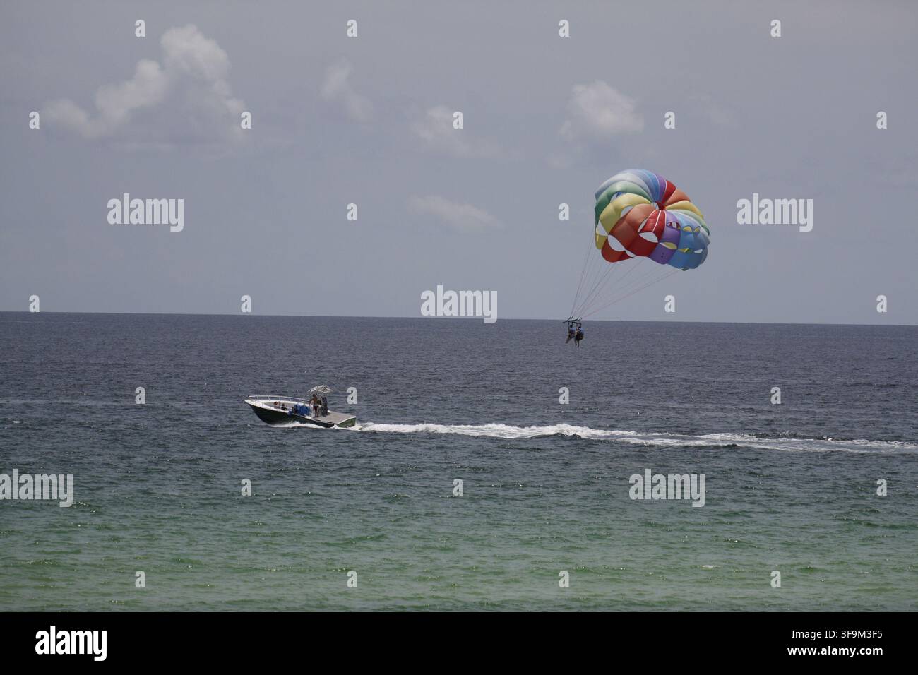 Des touristes enthousiastes décollent dans le ciel ensoleillé sous un parasail arc-en-ciel au-dessus des eaux émeraude de Destin, en Floride. Banque D'Images