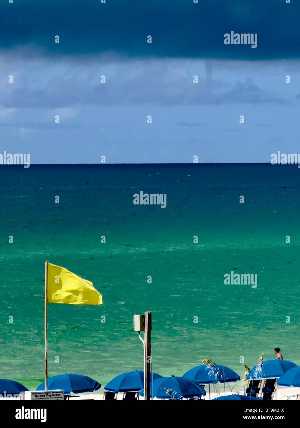Drapeau de sécurité jaune sur la plage de sable de Destin, en Floride, avec le golfe du Mexique calme sous un ciel gris bas et couvert. Banque D'Images