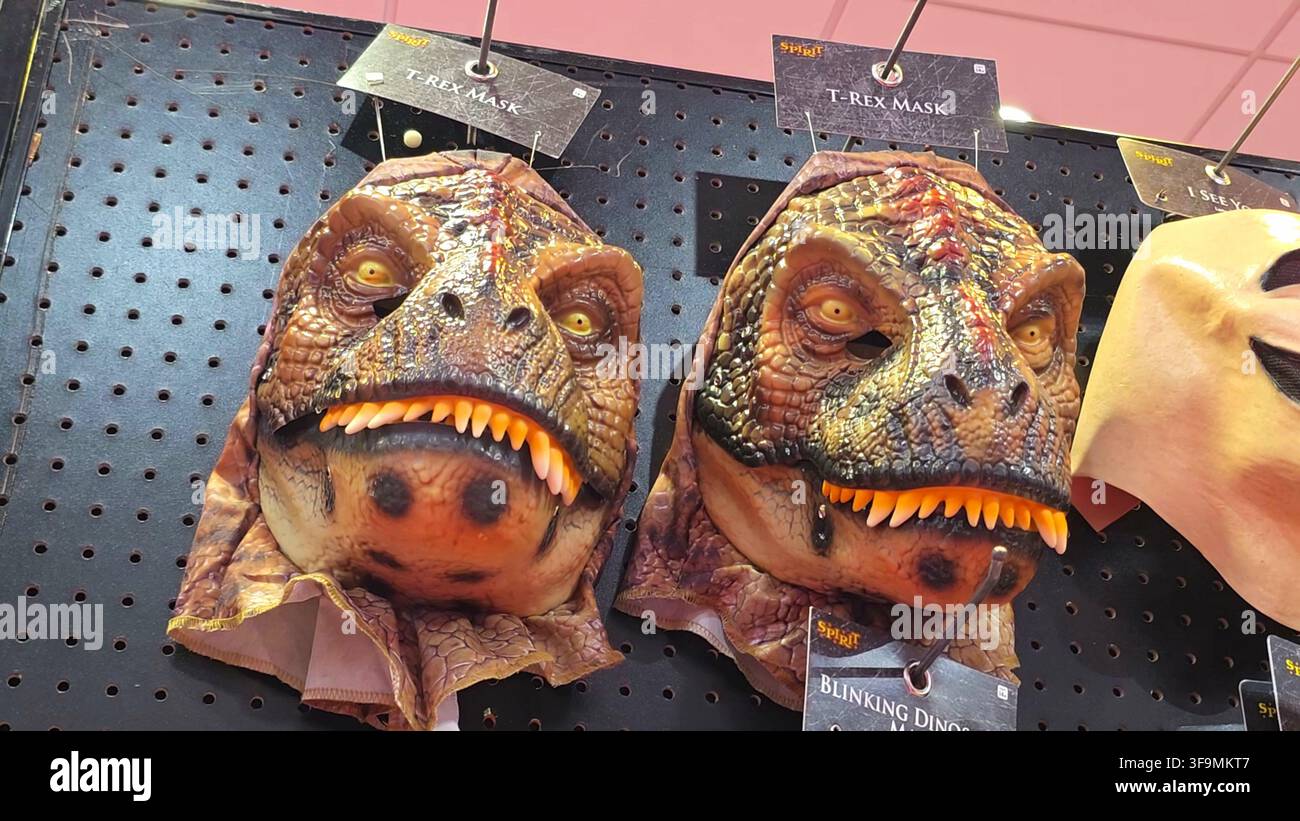 MEDINA, OH, ÉTATS-UNIS - 15 AOÛT 2026 : Gros plan de masques d’Halloween de dinosaures T-Rex exposés sur des crochets dans un magasin de détail pour les acheteurs de saison. Banque D'Images