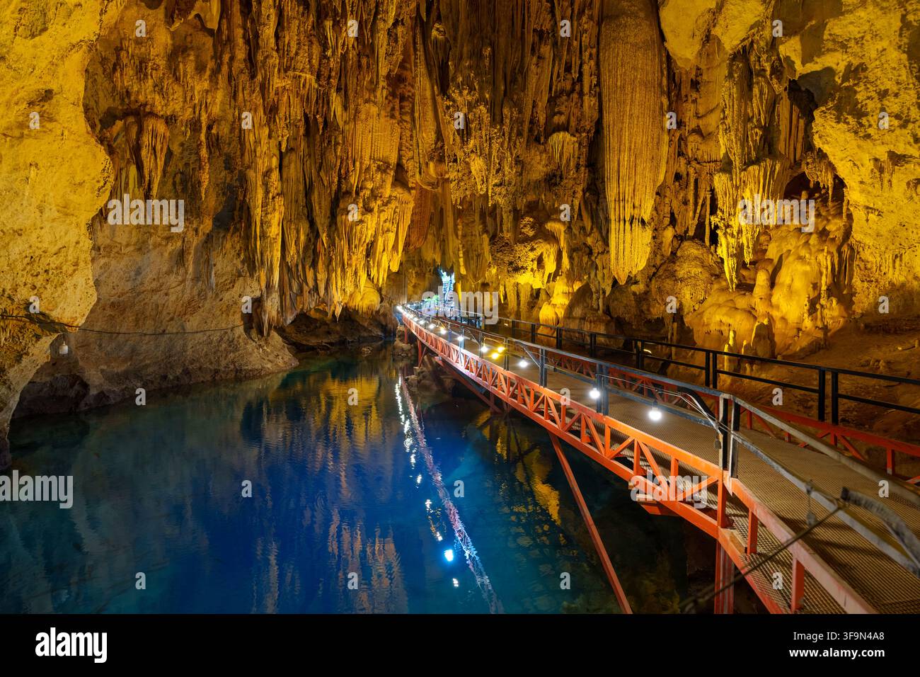 Une passerelle métallique éclairée traverse une piscine claire bleu-vert sous des formations de grottes suspendues denses. Banque D'Images