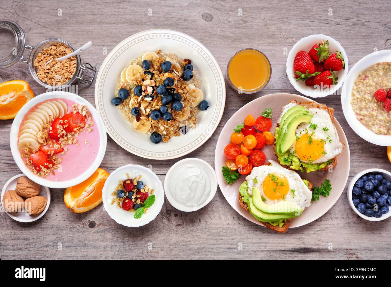 Scène de table pour un petit-déjeuner ou un brunch sain sur un fond en bois. Vue aérienne. Toast à l'avocat, bols de smoothie, avoine, yaourt et une sélection de fo nourrissante Banque D'Images