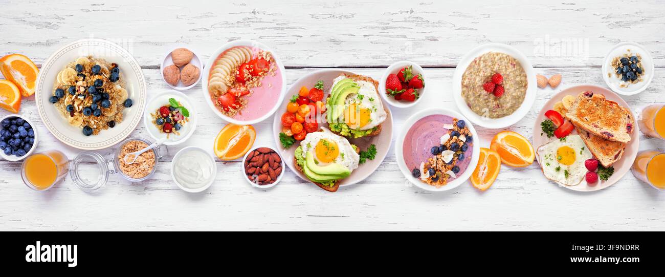 Scène de petit-déjeuner ou brunch sain sur un fond de bannière en bois blanc. Vue aérienne. Toast à l'avocat, bols de smoothies, avoine, yaourt et une variété de Banque D'Images