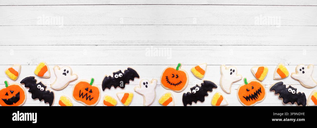 Bordure inférieure en biscuit pour Halloween. Vue de dessus sur un fond de bannière en bois blanc avec espace de copie. Fantômes, chauves-souris, lanternes jack-o et bonbons au maïs. Banque D'Images