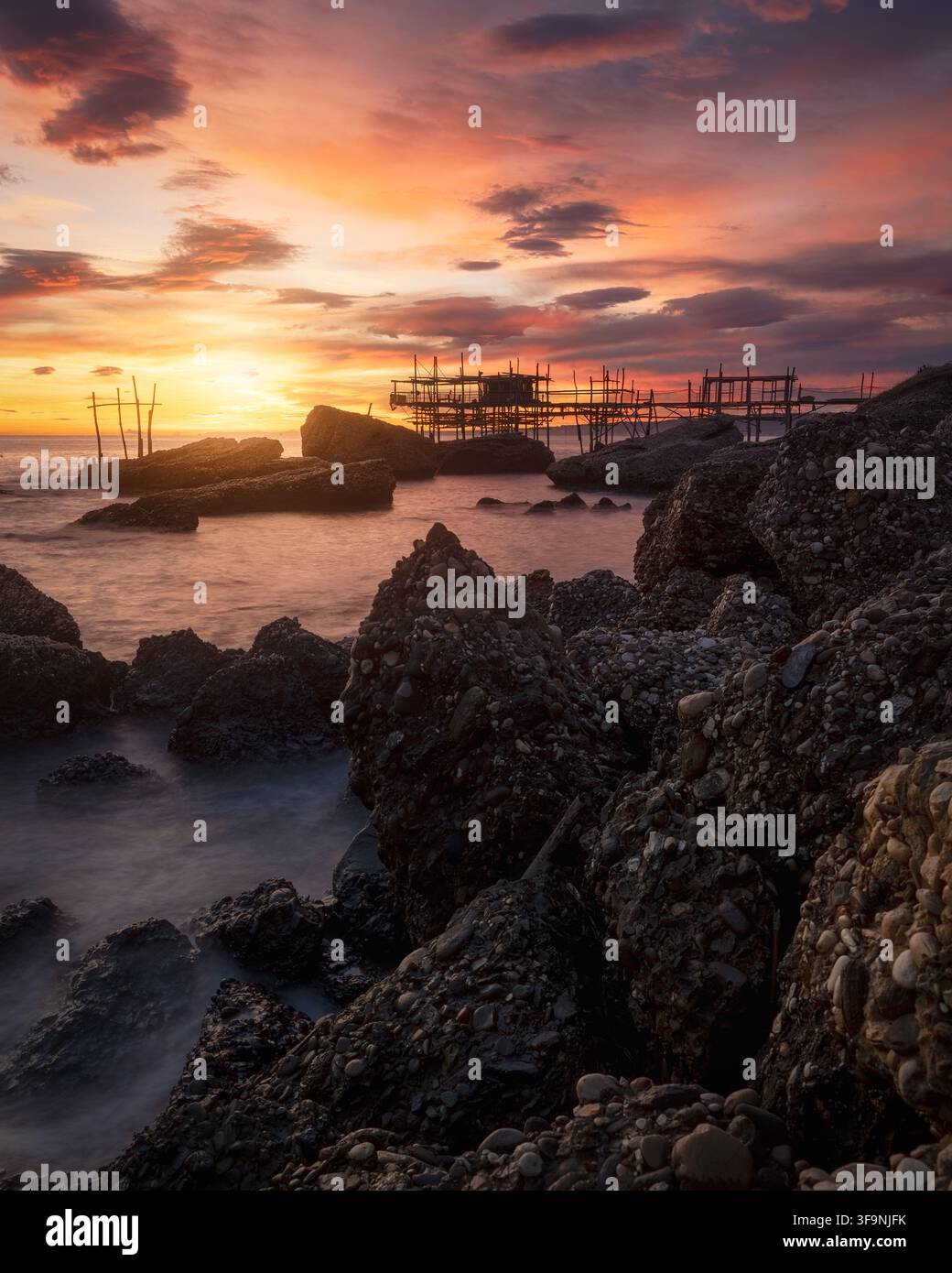 Vue de la structure de pêche historique Trabocco Spezzacatena se détachant sur un coucher de soleil éclatant au-dessus de la côte rocheuse de Rocca San Giovanni, Prov Banque D'Images