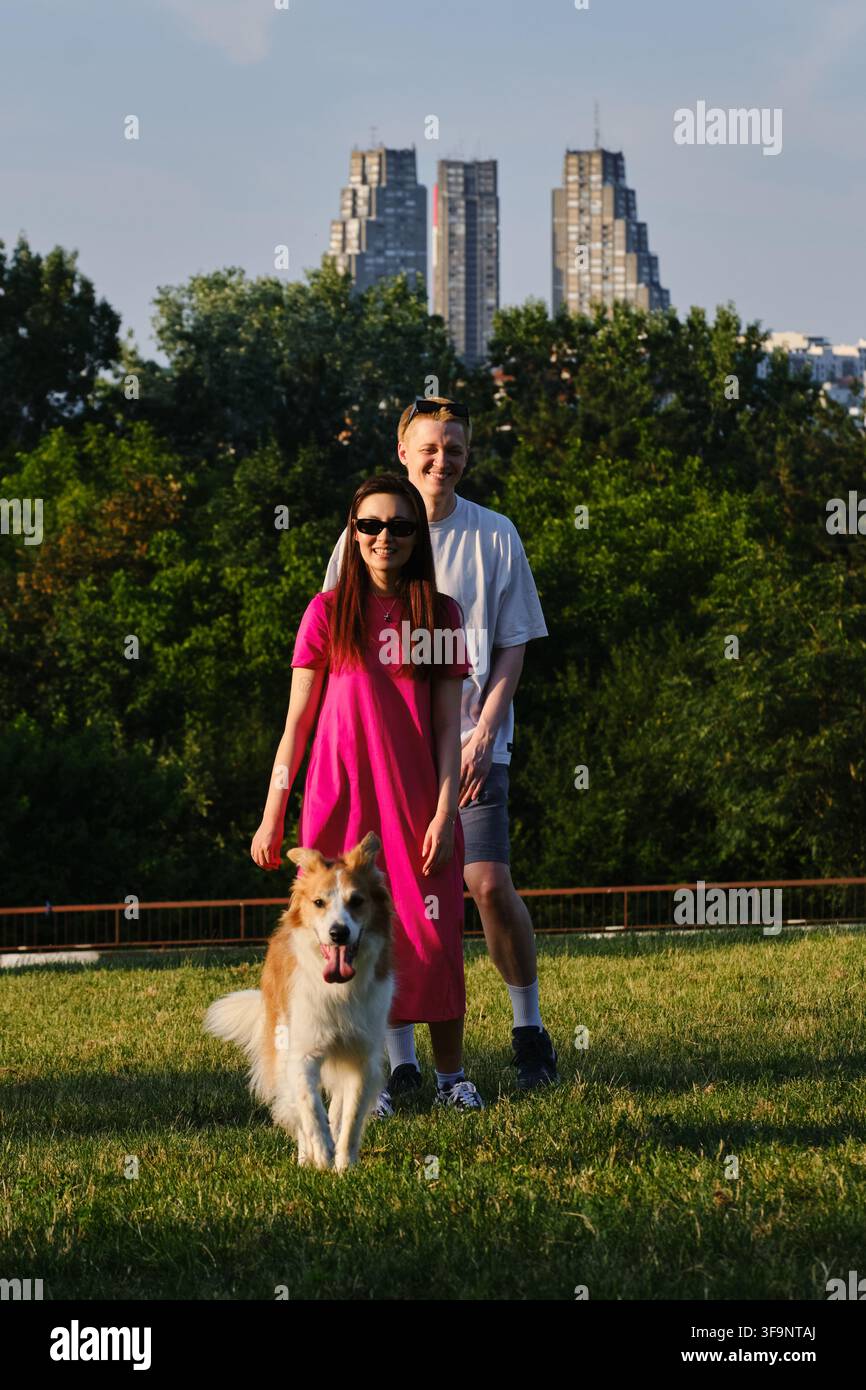 Chien courant sur l'herbe avec un couple heureux qui s'embrasse en arrière-plan. Animaux de compagnie, amour et style de vie en plein air. Banque D'Images